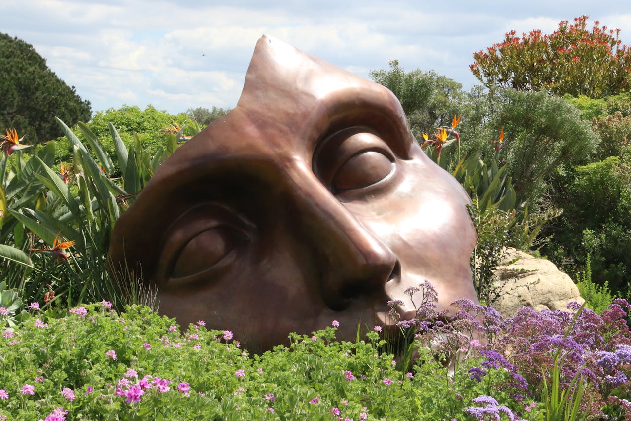 Bronze face sculpture nestled in a vibrant garden full of diverse flowers in Cape Town.