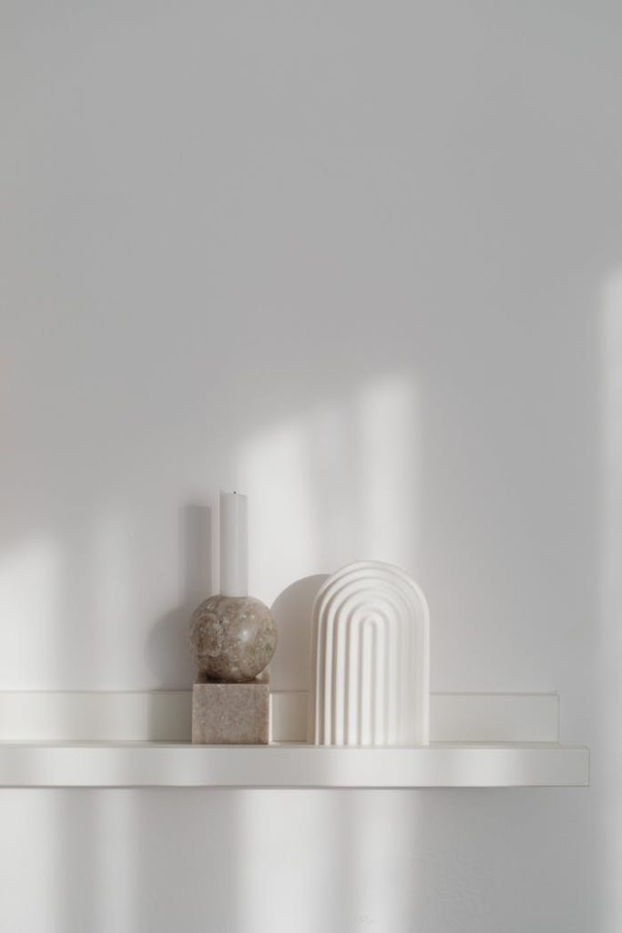 A minimalist shelf featuring a candle holder and modern sculpture against a soft-lit wall.