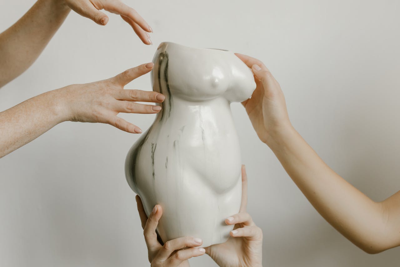 Hands gently holding and interacting with a uniquely shaped ceramic pottery piece indoors.